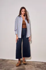 Camisa de corte oversize con estampado de rayas verticales en tonos azul claro y mostaza. Presenta cuello clásico, cierre frontal con botones y mangas largas con puños abotonados.
