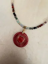 Collar de piedras naturales facetadas en tonos multicolor, con dije central de cerámica artesanal en forma de corazón rojo sobre base circular texturada y detalles en dorado.