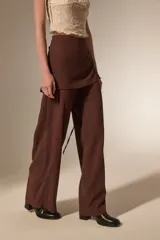 Pantalon de corte recto y tiro alto, confeccionado en tela texturizada color marrón, con detalle de falda superpuesta en la cintura.