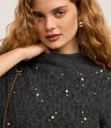 Buzo de tricot texturizado color gris con perlas blancas aplicadas. Tiene mangas largas abullonadas y cuello redondo.