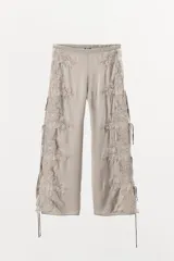 Pantalón de tiro alto confeccionado en tejido satinado color beige. Presenta pernera recta, cintura elástica y aberturas laterales ajustables con lazadas. Incluye aplicaciones de encaje a tono en los laterales.