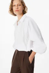 Camisa de corte holgado color marrón chocolate, con cuello clásico, cierre frontal de botones y mangas largas abullonadas con frunces en los hombros.