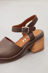 Sandalia de cuero marrón con diseño open-toe, tira ancha en el empeine, correa ajustable con hebilla en el tobillo y tacón ancho de madera.