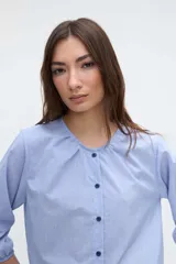 Camisa de manga larga con diseño a rayas celestes y blancas, cuello redondo y cartera de botones frontales. Presenta mangas con puños elásticos.
