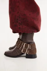 Bota de caña baja confeccionada en cuero con textura crocco, color bordó. Presenta taco cuadrado, punta cuadrada y un accesorio desmontable con doble hebilla metálica y tachas decorativas.