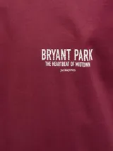 Remera de manga corta y cuello redondo, color rojo tibetano, con ajuste relajado. Presenta un estampado pequeño en el pecho con el texto "BRYANT PARK THE HEARTBEAT OF MIDTOWN".