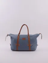 Bolso de viaje tipo duffle, confeccionado en cuero natural color azul con textura, con detalles de correas y asas en cuero color suela. Cuenta con cierre superior, bolsillo interior con cierre y compartimento para celular.