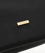 Cartera grande Satinato de color negro, confeccionada en poliéster con detalles en policloruro de vinilo. Posee un diseño moderno con cierre superior, bolsillo frontal con cierre visible y herrajes metálicos dorados, incluyendo una correa ajustable con hebillas y una placa con el logo de la marca.
