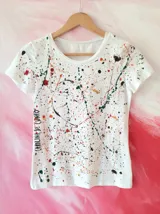 Remera blanca con estampado multicolor estilo salpicadura de pintura y texto lateral de la marca Carolina de Cunto, de manga corta y cuello redondo.