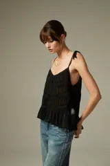 Musculosa negra de breteles finos, confeccionada en algodón con diseño plisado y detalles de encaje. Presenta un corte holgado con volados en el ruedo y escote profundo.
