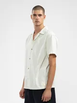 Camisa de manga corta color crema, con cuello camp y calce relajado. Confeccionada en una mezcla de lino y algodón, con botones de madera y parche característico de Polonio.