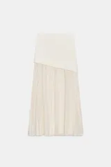 Falda midi color blanco roto o crema, de tiro medio. Presenta una sección superior lisa y ajustada, superpuesta a una sección inferior plisada y fluida.