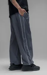 Pantalón deportivo de corte regular confeccionado en microfibra opaca, con cintura elástica y puños ajustables en los tobillos. Presenta vivos laterales a contratono que recorren toda la pierna y un pequeño parche con logo en el frente.