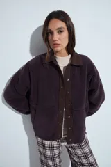 Campera de corderito color marrón oscuro, con cuello camisero y cartera frontal en tela lisa a tono. Presenta cierre mediante botones a presión y mangas largas con puños elásticos.
