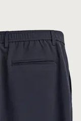 Pantalón de corte slim fit y color negro, confeccionado en tejido elástico. Cuenta con cintura elástica, trabillas, bolsillos frontales y cierre con cremallera y botón.