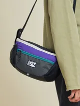 Bandolera negra con diseño técnico, confeccionada en poliamida con textura de cuadrícula. Cuenta con doble cierre frontal, bolsillos laterales de malla y correa ajustable. Incluye el logo de la marca Rusty en el frente.