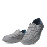 Championes tipo mocasín slip-on Merrell Hut Moc 2, color gris con diseño acolchado tipo matelassé. Presenta talón colapsable, suela de EVA ligera y detalles en azul en la parte posterior.