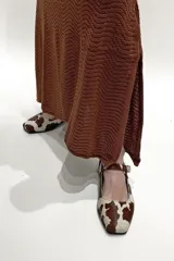 Zapato Mary Janes de cuero con estampado de vaca en tonos marrón y blanco, con correa sobre el empeine y hebilla metálica.