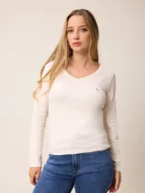 Remera de manga larga color beige, con cuello en V y un pequeño logo bordado en rosa en el pecho.