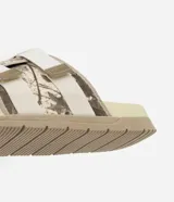 Ojota tipo slide con estampa camuflada en tonos beige y marrón. Presenta dos tiras ajustables con cierre de velcro y suela de goma antideslizante.