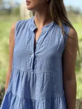 Vestido celeste de lino, sin mangas, con cuello mao y botones de nácar. Presenta varios cortes en su largo, aportando movimiento y un toque moderno a este diseño fresco y elegante.