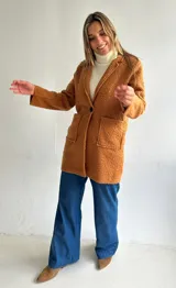 Abrigo estilo sastrero de textura tipo bouclé en color camel, con cierre frontal de un botón, solapas clásicas y bolsillos frontales tipo plaqué.