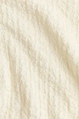 Top blanco de punto texturizado, con manga japonesa, cuello alto y abertura con botón en la nuca.