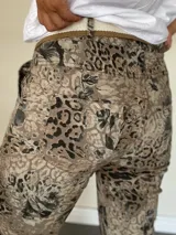 Pantalón de mujer con estampado animal print en tonos marrones y negros, de corte ajustado y largo hasta el tobillo. Incluye un cinturón de tela a rayas blancas y marrones.