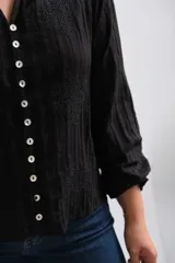 Blusa negra de manga larga con cierre frontal de botones, cuello mao y textura sutilmente rayada con detalles bordados.