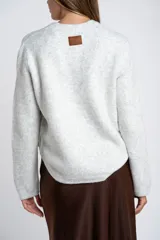 Sweater de punto gris melange con cuello redondo, manga larga y detalle de botones laterales en el costado.