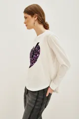 Remera de manga larga color blanco con estampa frontal de un corazón con diseño animal print en tonos violeta y negro, atravesado por un rayo negro.