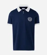 Polo de manga corta color azul marino con cuello y bordes de mangas en color blanco. Presenta cierre frontal parcial y escudo bordado en el pecho.