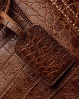 Bolso shopper negro de cuero con textura de cocodrilo, doble asa de hombro y dije colgante rectangular.