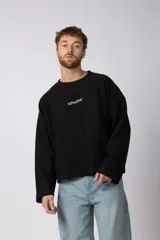 Buzo de cuello redondo confeccionado en tejido rústico con bordes al corte y costuras expuestas. Presenta un diseño boxy con estampado frontal y es reversible, permitiendo su uso por ambos lados.