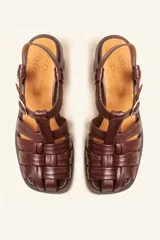 Sandalias de cuero color negro con diseño de tiras cruzadas tipo huarache, tira ajustable con hebilla metálica en el empeine y taco cilíndrico de madera.