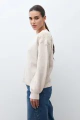 Sweater de punto en color beige melange, con cuello redondo y mangas largas. Presenta apliques de flores tejidas en relieve sobre los hombros y el pecho.