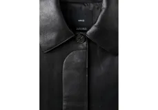 Chaqueta de cuero sintético color negro, con cuello camisero, cierre frontal oculto y mangas largas con puños rectos.