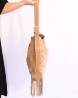 Cartera tipo shoulder bag de cuero gamuzado color suela, con diseño de flecos en la base y detalle de tachas metálicas en los laterales. Cuenta con correa regulable y forro interior.