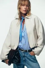 Chaqueta bomber negra con cuello solapa, manga larga abullonada y puños elásticos. Presenta falsos bolsillos de doble vivo en la parte delantera y cierre frontal con cremallera.