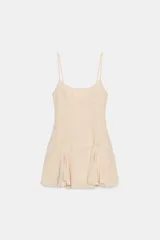 Vestido corto estilo lencero color beige, con escote redondo, tirantes finos ajustables y detalles de encaje y bordados a tono. Presenta un diseño con costura horizontal en la cintura y bajo acabado con volantes.