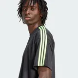 Remera de corte holgado Adidas Adicolor Jacquard, color negro con detalles en verde lima brillante en el logo del pecho y las clásicas tres tiras en los hombros y mangas. Presenta un sutil diseño de rayas verticales tipo jacquard.
