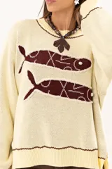 Buzo tejido de punto en color manteca, con diseño frontal de dos sardinas en color bordó. Presenta detalles bordados a mano en los bordes de las figuras y terminaciones con galón picot en cuello, puños y ruedo. Posee un corte holgado y aberturas laterales en el bajo.