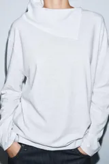 Camiseta blanca de manga larga con cuello redondo y superposición de tela tipo pañuelo.