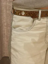 Cinto de cuero con estampado animal print, decorado con tachas metálicas, remaches y ojales plateados. Cuenta con una hebilla metálica cuadrada en tono bronce envejecido.