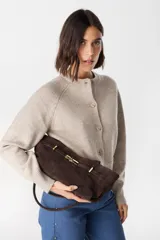 Bolso de hombro confeccionado en cuero vacuno color bordó, con textura granulada. Presenta un diseño estructurado con una solapa frontal decorativa que incluye un cierre metálico tipo torniquete en tono dorado.