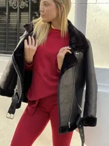 Campera tipo gamulán de cuero sintético negro con interior y detalles de corderito al tono. Presenta cierre frontal diagonal, cuello amplio, bolsillos laterales con cierre y cinturón ajustable en el ruedo.