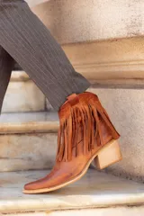 Bota texana de caña corta color marrón, fabricada en cuero con forro de cuero. Presenta cierre lateral y flecos en el tobillo.