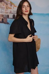 Vestido camisero negro de lino con diseño de encaje perforado, cuello clásico, cierre frontal con botones y mangas cortas acampanadas con frunces en los hombros.