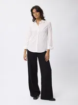 Camisa blanca de corte clásico, con cuello camisero, cierre frontal de botones y mangas largas con puños doblados.