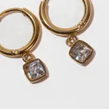 Aros tipo argolla dorados con dije cuadrado con piedra blanca.